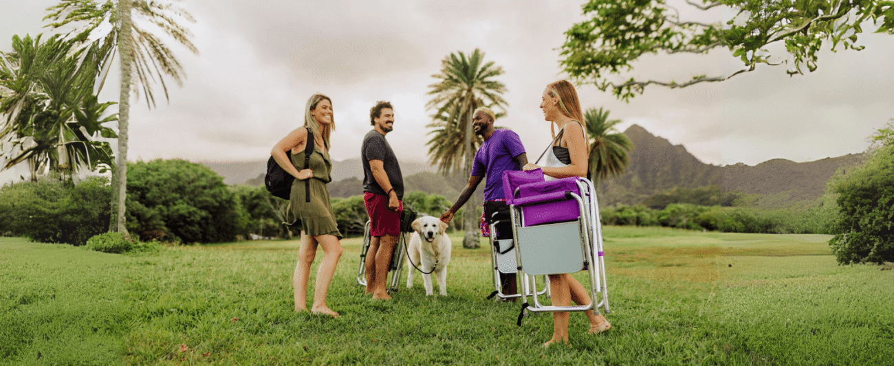 Multi-person tropical lawn leisure scene; carrying lightweight, foldable director's chairs (including purple and red models); interacting with a golden retriever background of palm trees and distant mountains; highlighting the portable and easy-to-carry features of the chairs; suitable for camping/picnicking/dog walking and other outdoor.