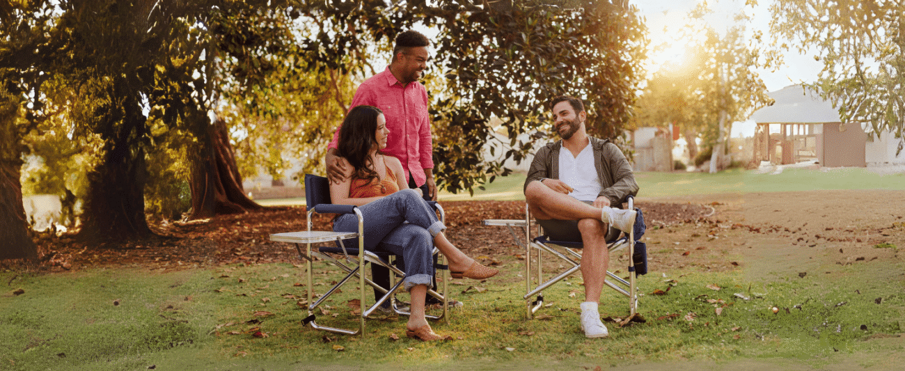 Multi-person lawn leisure scene under a tree, showcasing a camping director's chair with a folding tabletop, creating a relaxed and comfortable atmosphere, suitable for leisure scenarios such as picnics, camping, and garden gatherings, with natural light creating a warm and cozy feel.